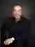 Aaron Gonzalez smiling in a black dress shirt, posed against a dark gray studio background.